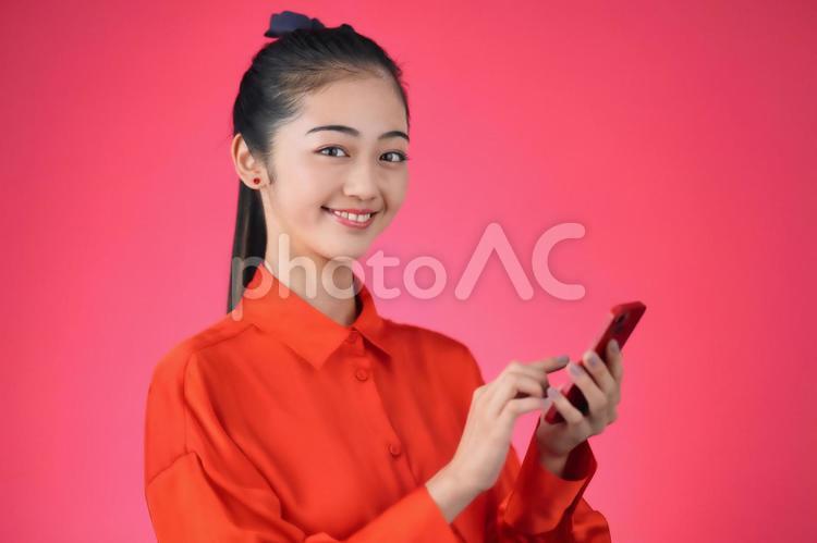赤色背景でスマホを使う女性 女性,日本人,ポートレートの写真素材