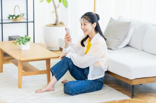 部屋でスマホを操作する女性 部屋でスマホを操作する女性 スマホ,笑顔,部屋の写真素材