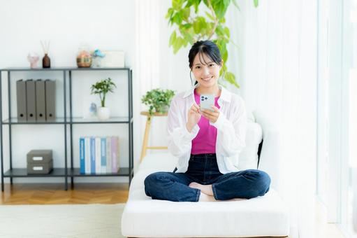 部屋でスマホを操作する若い女性 スマホ,笑顔,若い女性の写真素材