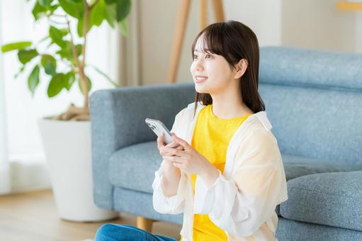 部屋でスマホを操作する若い女性 部屋でスマホを操作する若い女性 スマホ,若い女性,笑顔の写真素材