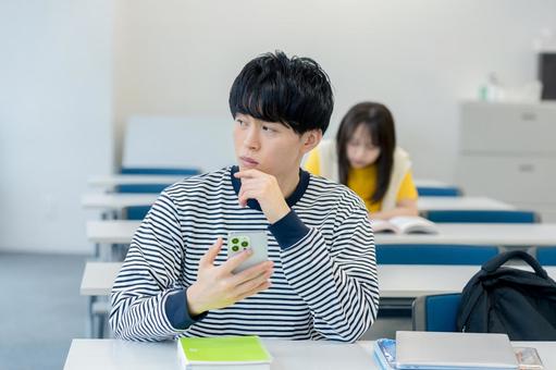 スマホを見ながら悩む大学生 スマホ,大学生,男性の写真素材