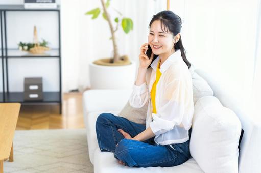 リビングでスマホで話す若い女性 リビングでスマホで話す若い女性 スマホ,笑顔,電話の写真素材