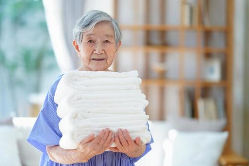 タオルを重ねて持つカメラ目線のおばあちゃん 女性,タオル,持つの写真素材