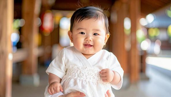 白い産着に包まれて笑顔の日本人の赤ちゃんの写真