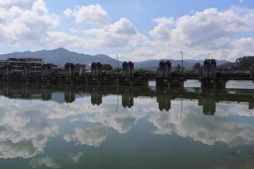 空と山と洗堰のうつる川の水鏡の水面の風景 空と山と洗堰のうつる川の水鏡の水面の風景の写真