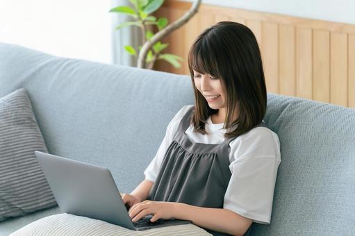 ソファに座ってパソコンを使う女性 ソファに座ってパソコンを使う女性 女性,ソファ,パソコンの写真素材