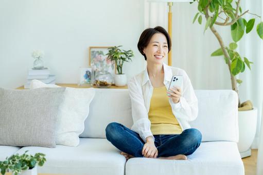 部屋でスマホを使うミドル女性 スマホ,笑顔,女性の写真素材