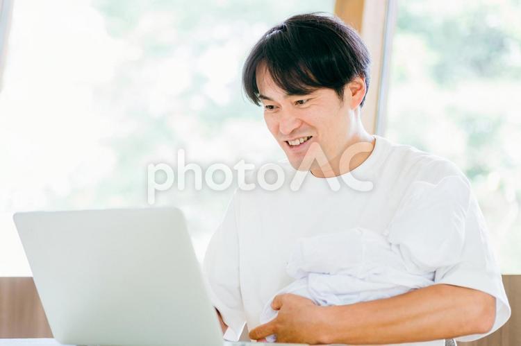 赤ちゃんを抱きながら仕事する男性 テレワーク,育児,リモートワークの写真素材