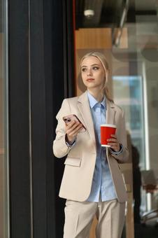 コーヒーとスマートフォンを持ってガラスの前に立つビジネスウーマン ビジネスウーマン,ビジネス,女性の写真素材