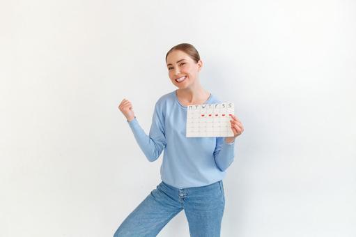 月経期間を示すカレンダーを手に持ちガッツポーズする女性（白背景） 生理,月経,女性の写真素材