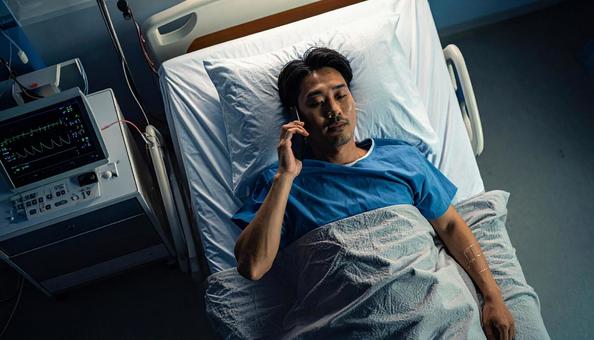 病室のベッドから携帯で話をする男性患者 病室のベッドから携帯で話をする男性患者の写真