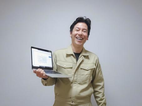 笑顔でノートパソコンを持つ作業服の男性 作業服,男性,笑顔の写真素材