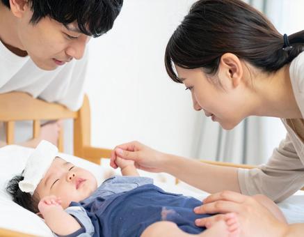熱を出す赤ちゃんを心配そうに見守る夫婦の写真