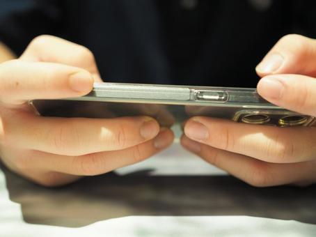 The hand of a young man holding a smartphone sideways, JPG