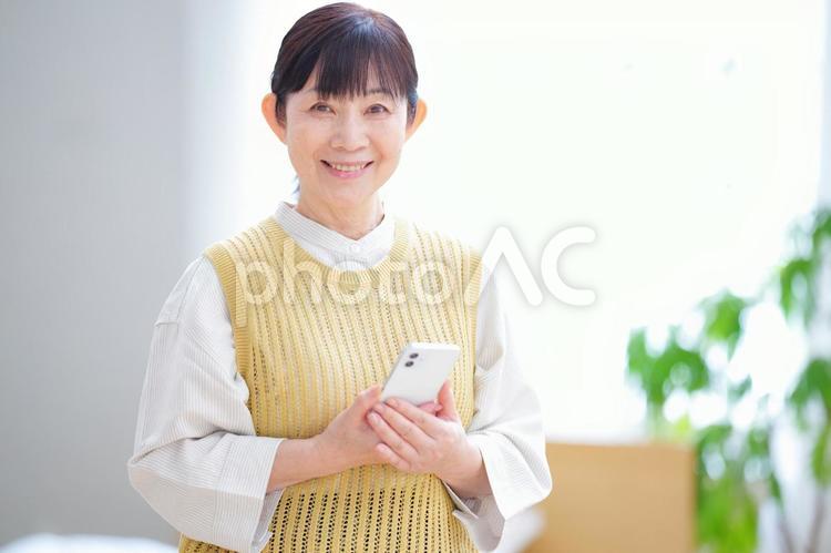 スマホを手に微笑む中年女性の室内ポートレート 主婦,家政婦,シニアの写真素材