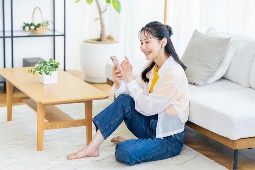 部屋でスマホを操作する女性 スマホ,笑顔,部屋の写真素材