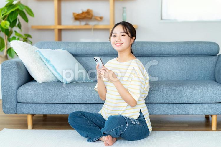 部屋でスマホを操作する若い女性 スマホ,若い女性,笑顔の写真素材