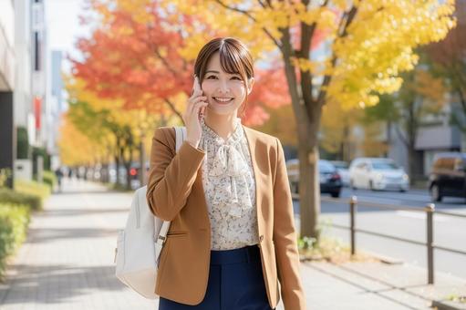 紅葉を背景にスマフォで会話する女性の写真