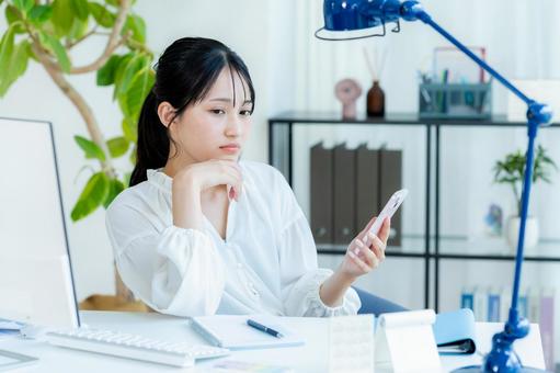 スマホを見ながら考えるビジネスウーマン スマホ,考える,悩むの写真素材