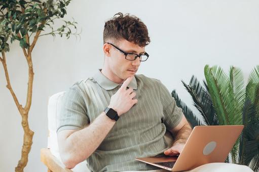 椅子に座って膝の上でノートパソコンを使うポロシャツを着た男性 男性,外国人,欧米人の写真素材