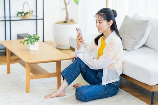 部屋でスマホを操作する女性 スマホ,笑顔,部屋の写真素材