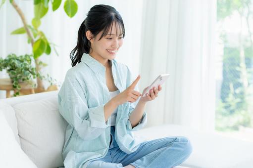 部屋でスマホを操作する若い女性 スマホ,笑顔,女性の写真素材