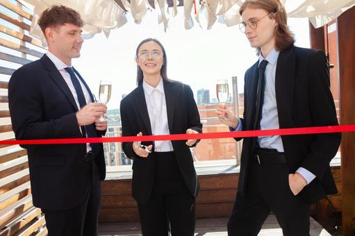 赤いテープの前に立つスーツの男女の写真