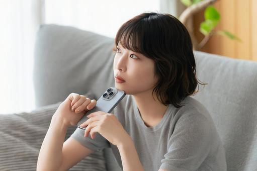 スマホを持って考えごとをする女性 スマホを持って考えごとをする女性の写真