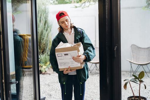 玄関で潰れた段ボール箱を持って立っている配達員の男性 配達,フードデリバリー,デリバリーの写真素材