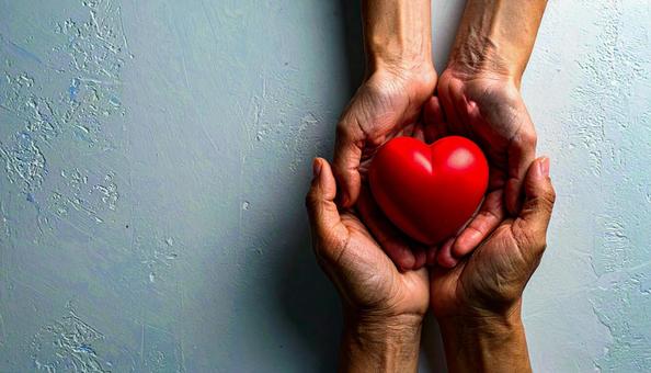 ハートを贈る　机の上でハートを握る両手の写真