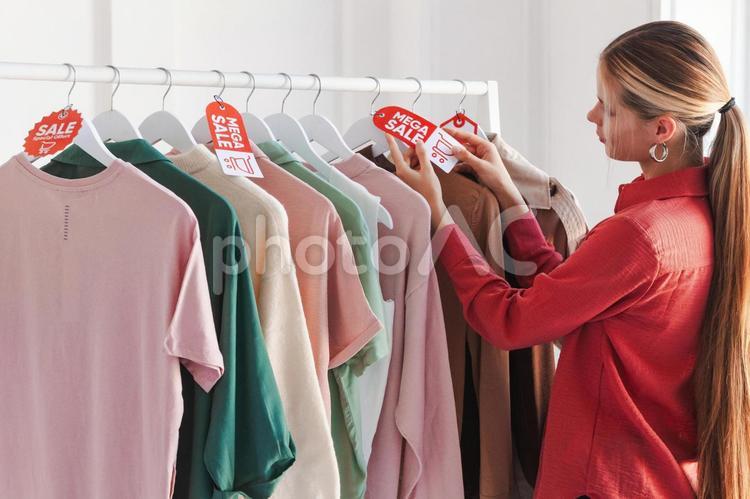 ハンガーに掛かった洋服のセールタグを触る女性 セール,ショップ,女性の写真素材