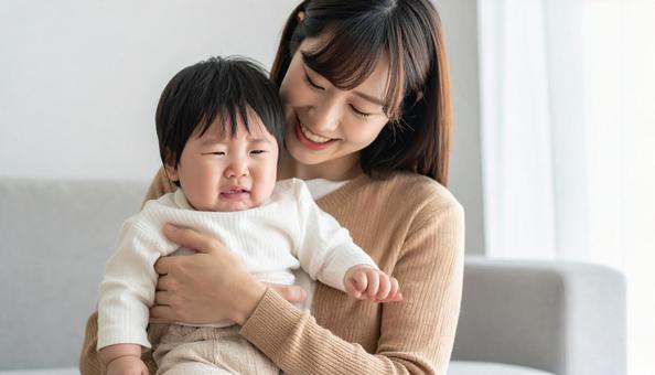 泣いている赤ちゃんを抱っこする笑顔の母親 泣いている赤ちゃんを抱っこする笑顔の母親の写真