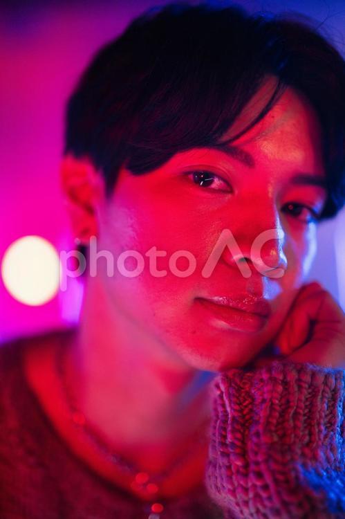 カメラ目線で頬杖をするピンク照明の男性アップ 男性,微笑む,頬杖の写真素材