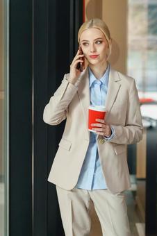 コーヒー片手に電話するビジネスウーマン ビジネスウーマン,ビジネス,女性の写真素材