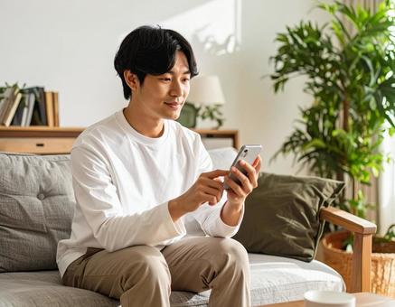 自宅でスマホを操作する若い男性 自宅でスマホを操作する若い男性の写真