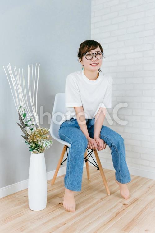 部屋で椅子に座るメガネをかけた日本人女性 メガネ,デニム,眼鏡の写真素材