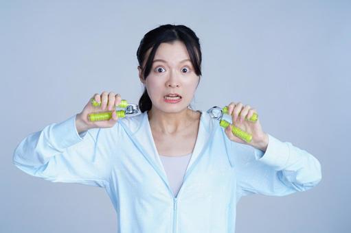 水色の服の女性が健康器具を口元に近づける 女性,ハンドグリップ,握るの写真素材