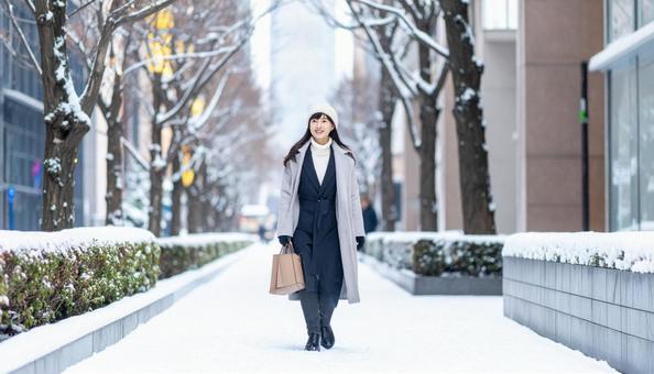雪の降るオフィス街を歩く笑顔の日本人女性 雪の降るオフィス街を歩く笑顔の日本人女性の写真