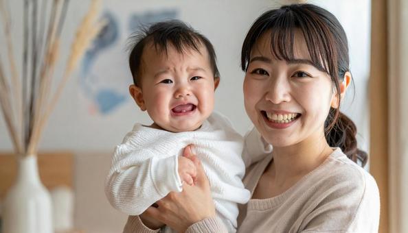 泣いている赤ちゃんを抱っこする笑顔の母親 泣いている赤ちゃんを抱っこする笑顔の母親の写真