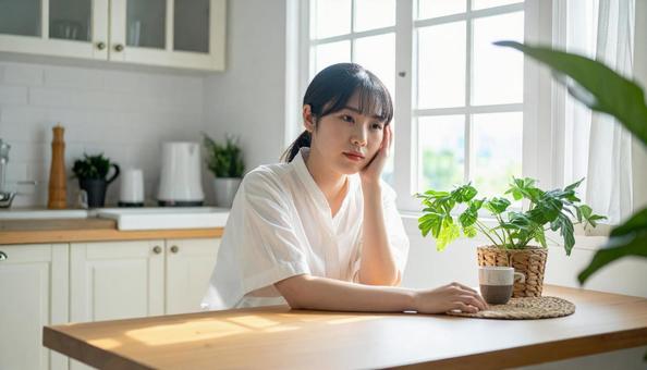 疲れた表情でキッチンに座る若い女性 疲れた表情でキッチンに座る若い女性の写真