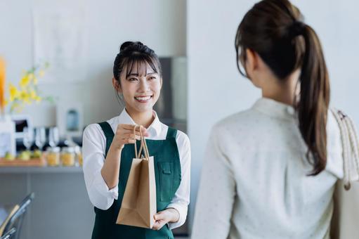 商品を渡す若い女性の店員 商品を渡す若い女性の店員の写真