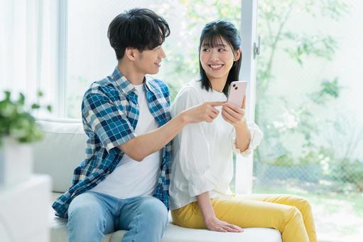 リビングでスマホを見るカップル リビングでスマホを見るカップル スマホ,笑顔,カップルの写真素材