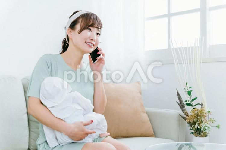赤ちゃんを抱っこしながら電話する女性 赤ちゃん,ママ,スマホの写真素材