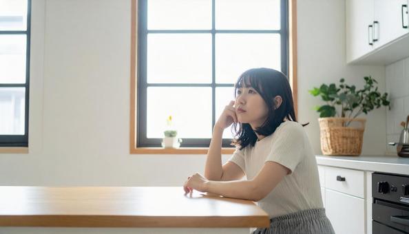 疲れた表情でキッチンに座る若い女性 疲れた表情でキッチンに座る若い女性の写真