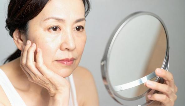 ほうれい線を気にしてほほを触る中年の女性 ほうれい線を気にしてほほを触る中年の女性の写真