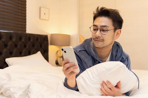 ベッドで寝そべりながらスマホを使う男性 ベッドで寝そべりながらスマホを使う男性 男性,人物,日本人の写真素材