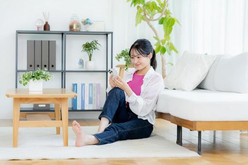 部屋でスマホを操作する若い女性 スマホ,笑顔,若い女性の写真素材