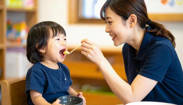 子どもにご飯をあげる保育士の写真
