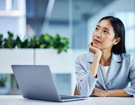 パソコンの前で考える女性社員 パソコンの前で考える女性社員の写真