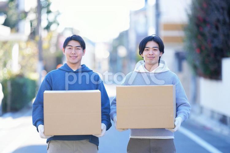 屋外で引っ越しの段ボール箱を持って並んで立っている2人の男性 引っ越し,一人暮らし,男性の写真素材